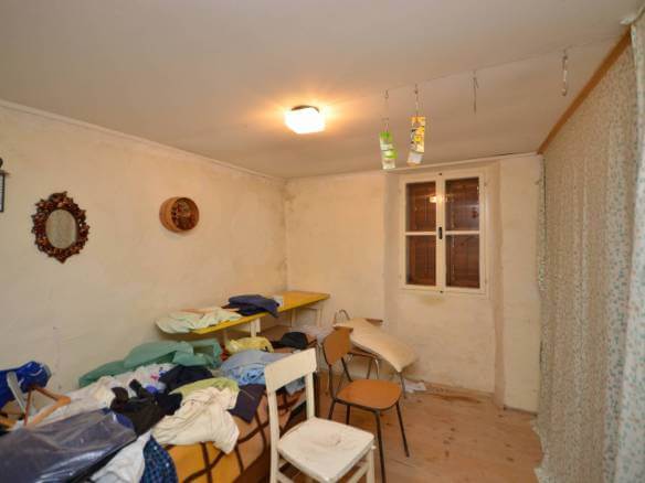 Neurejena soba z oblačili, naloženimi na mizah in stolih, visečo vrvjo za perilo s sponkami, majhnim oknom in okrasnim ogledalom na steni.