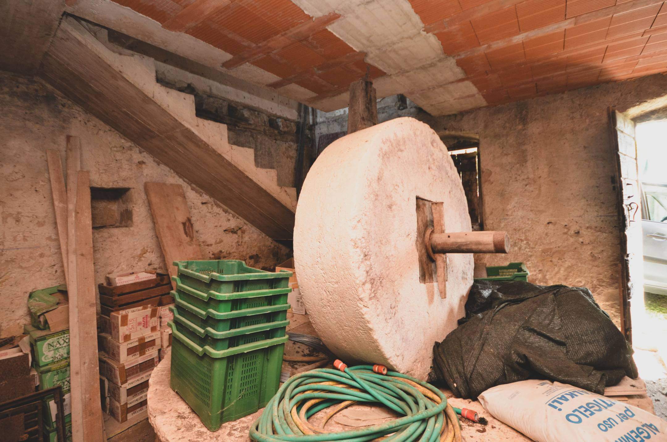 Notranji prostor za shranjevanje gradbenih materialov z zelenimi plastičnimi zaboji, lesenimi deskami, cevmi in velikim okroglim mešalnikom za cement na grobi steni.